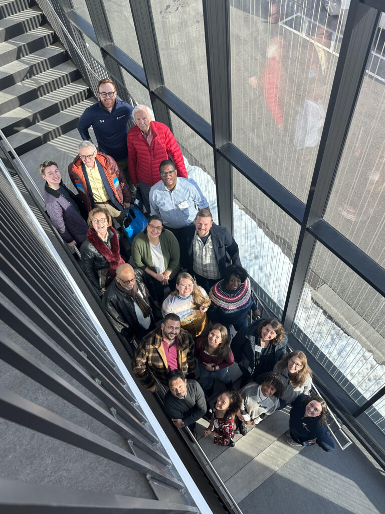 An aerial shot of the Alumni Board members gathered on a flight of stairs, smiling up at the camera