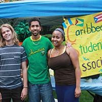 Photo of three students smiling in front of a poster for Caribbean Student Association