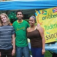 Photo of three students smiling in front of a poster for Caribbean Student Association