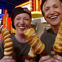 Photo of two women smiling and holding fried dough on a stick