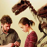 Photo of two people talking in front of a dinosaur skeleton