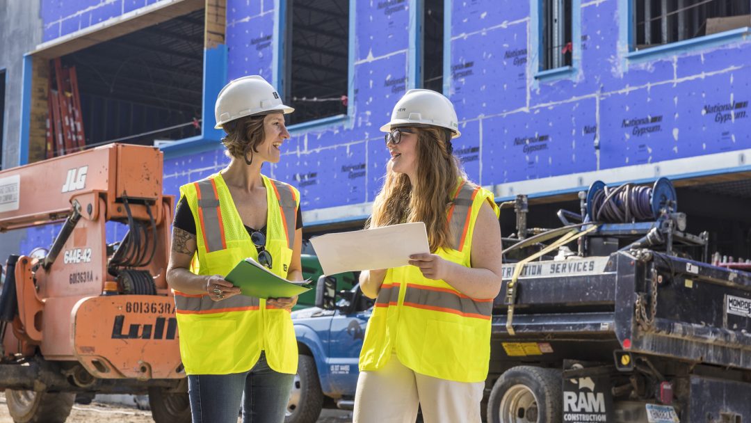 Wearing a hard hat and neon yellow work vest, student Annabel Gregg works on-site at the construction of the new Family Tree Clinic. Construction equipment is seen in the background.
