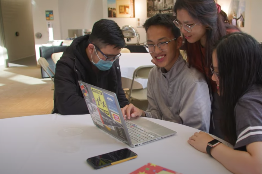 A team of four students smiles as they look at a laptop during Macathon 2021.