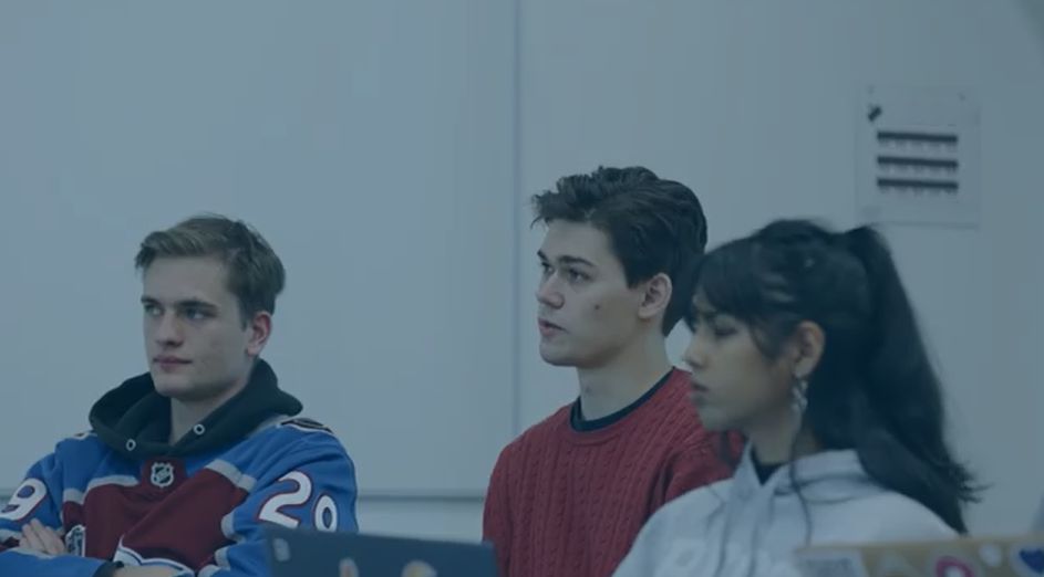 Three students sit in a classroom, looking at something off camera.