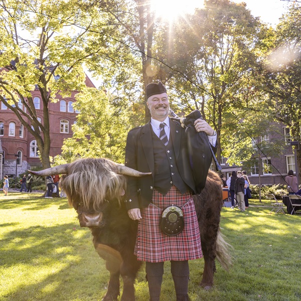 One of Macalester's bagpipers standing with a highland cow.