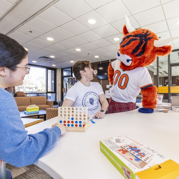 Macalester Mascot and students playing connect4 in student lounge