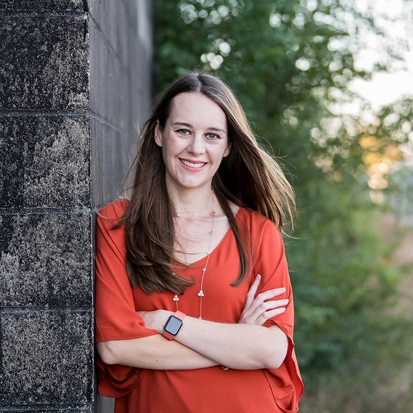 Kate Agnew ‘11, Senior Director of Engineering at Marriott International, leans against a dark concrete wall with her arms crossed, smiling brightly.