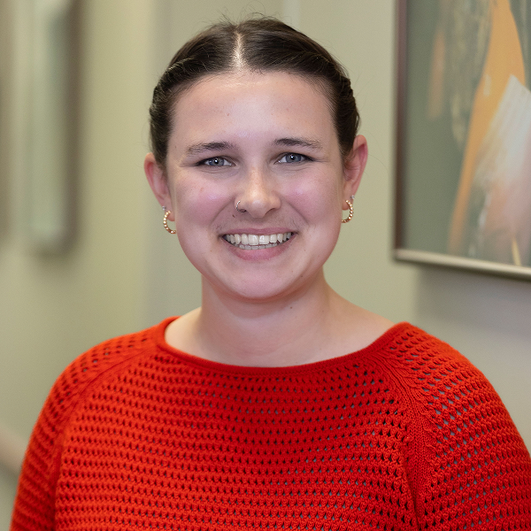 Mara Steinitz ’18, wearing a bright orange mesh-knit sweater, smiles in an indoor headshot