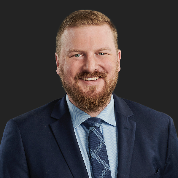 Matthew Bergeron ’08, a Shareholder at Larkin Hoffman, smiles in a professional headshot wearing a navy suit and a blue patterned tie against a dark background.