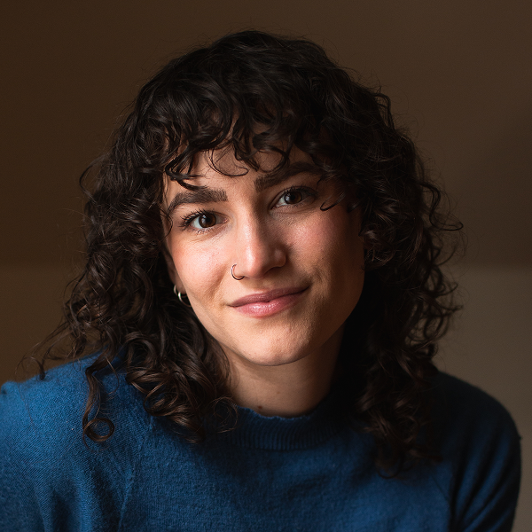 Miriam Moore-Keish ’19, Content Strategist at Capstone Publishing, smiles in a headshot with curly dark hair and a nose ring, wearing a blue sweater.