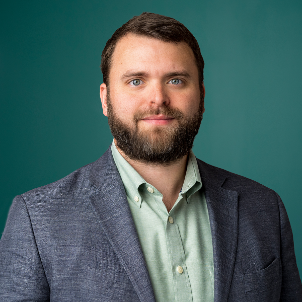 Samuel Dolce ’14, Attorney and Partner at Milestone, looks forward in a professional headshot, wearing a blazer and a light green shirt against a teal background.