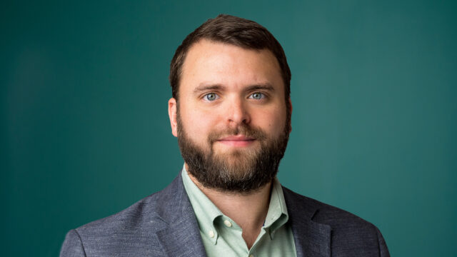 Samuel Dolce ’14, Attorney and Partner at Milestone, looks forward in a professional headshot, wearing a blazer and a light green shirt against a teal background.