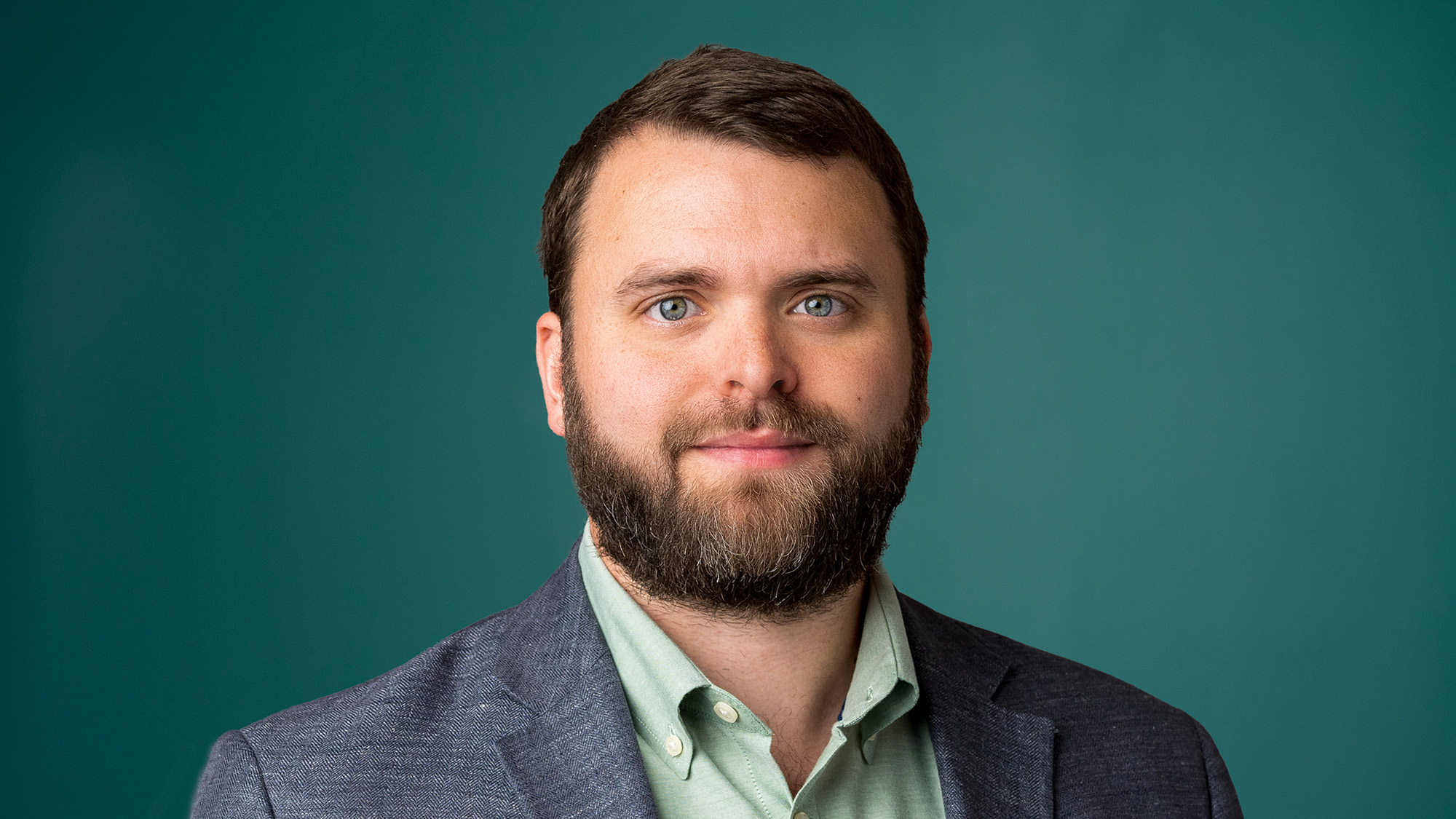 Samuel Dolce ’14, Attorney and Partner at Milestone, looks forward in a professional headshot, wearing a blazer and a light green shirt against a teal background.