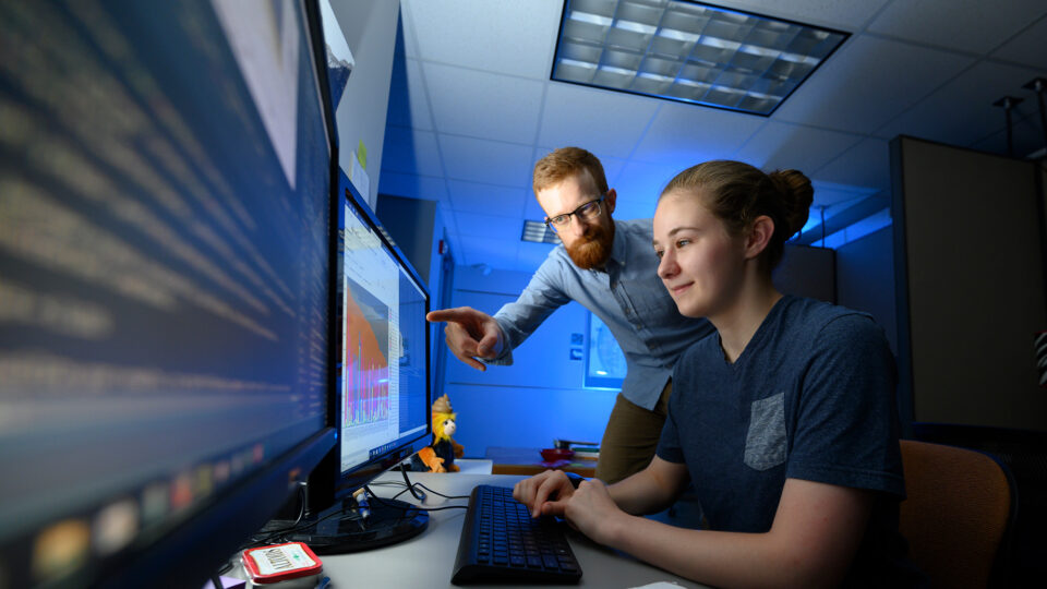 A biology student and professor work together at a computer.