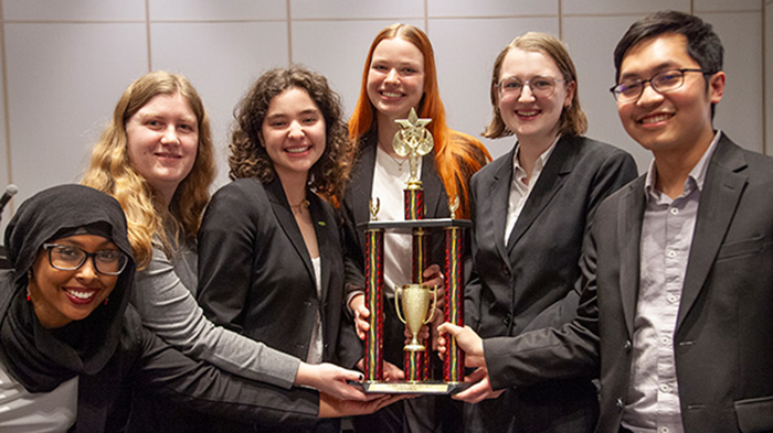 6 students dressed in suits hold an Ethics Bowl trophy
