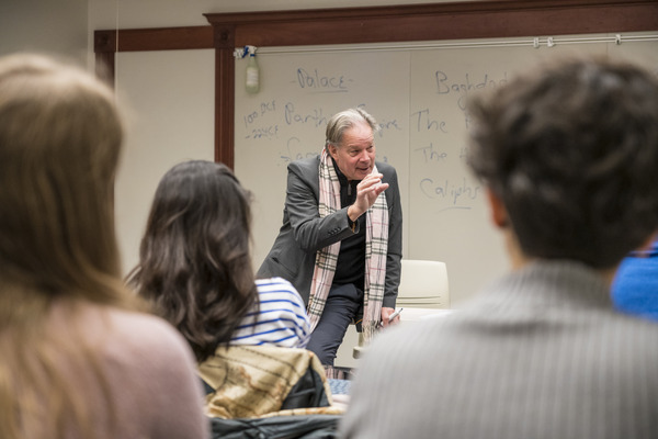 Professor sits on a desk in front of a classroom and teaches seated students