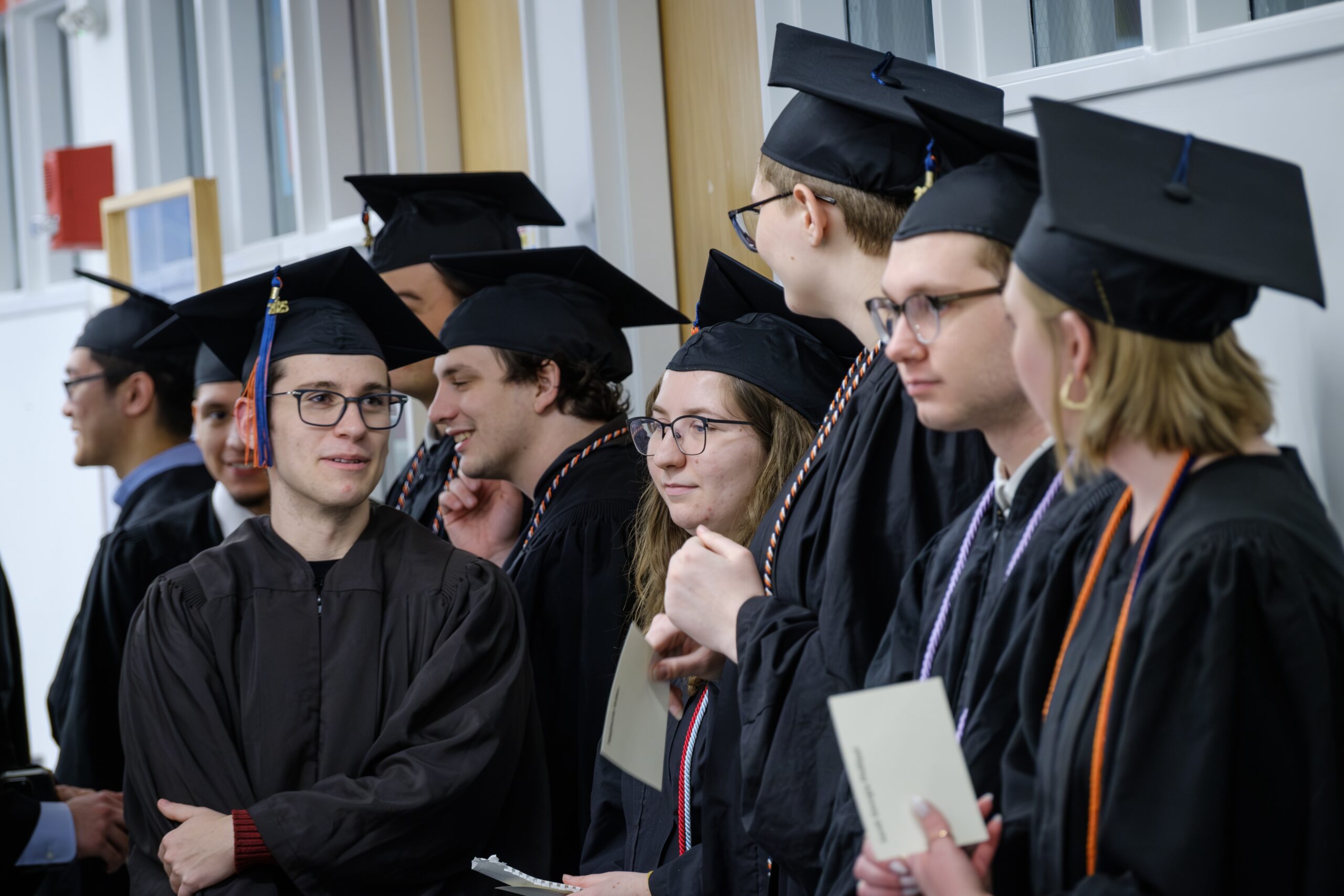 Students in black graduation caps and gowns lined up to process into the December, 2024 commencement celebration.