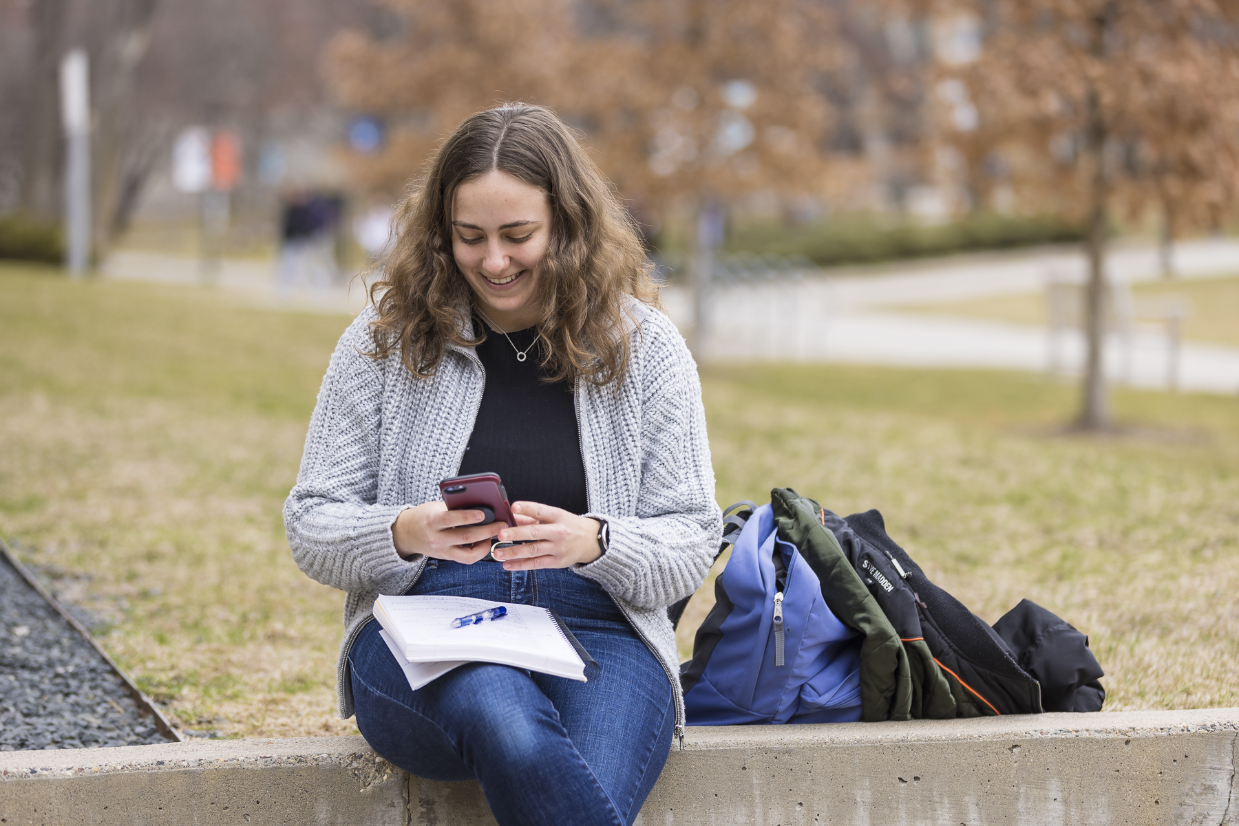 A female student sits outside while checking their cell phone.