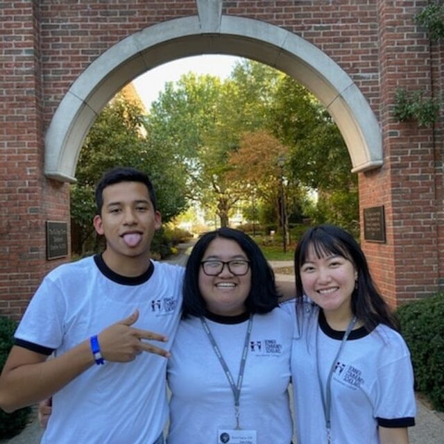 Three students wearing matching T-shirts smile