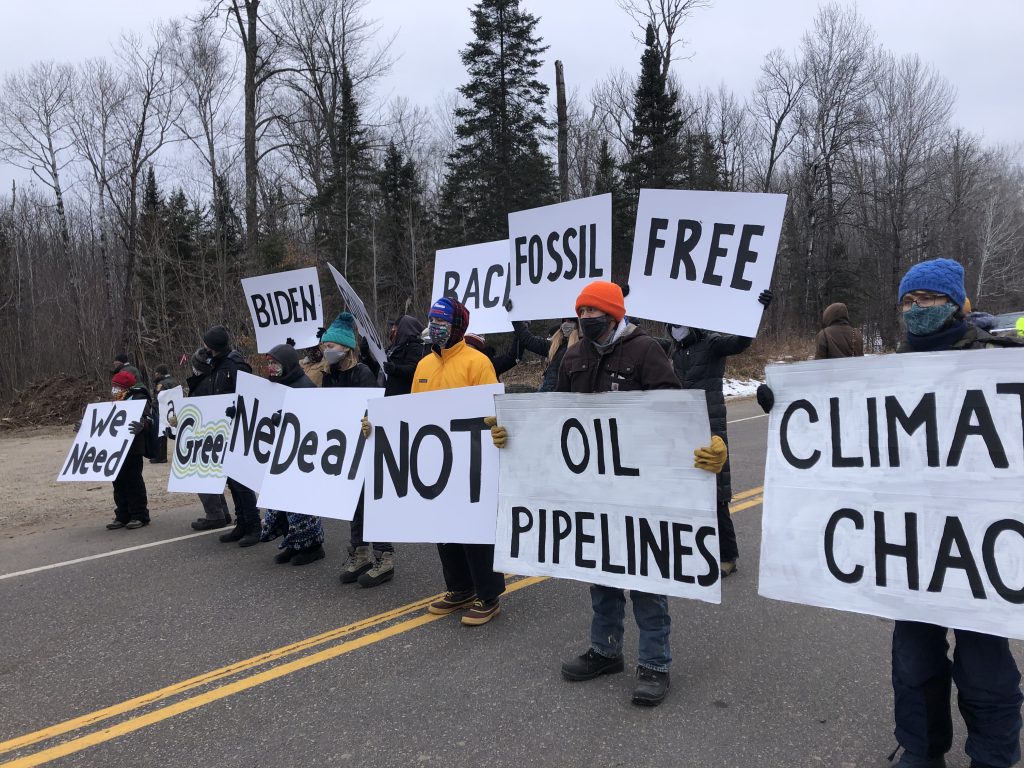 Protesters hold signs near a proposed Line 3 pipeline route.