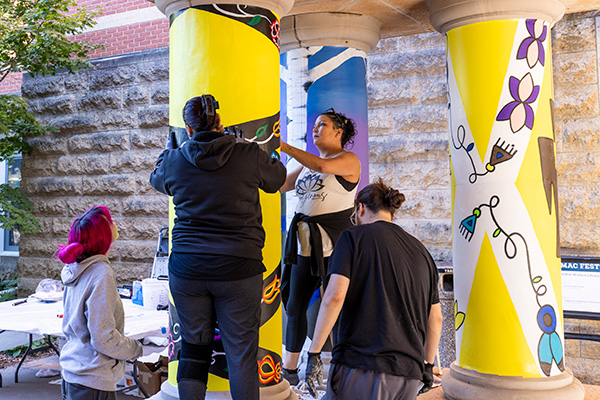 Four people work on painting a yellow pillar