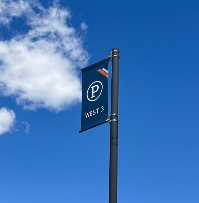 A navy blue banner on a pole that has a white circled P for parking in the center and reads West 3 underneath. The background is the blue sky.