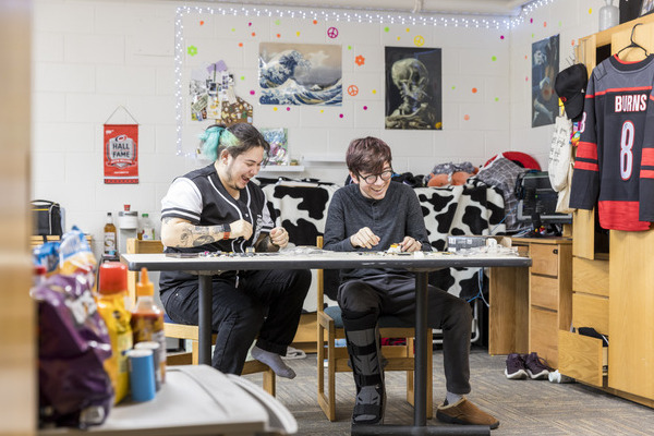 Two roommates sit in a dorm room putting together Lego blocks and laughing