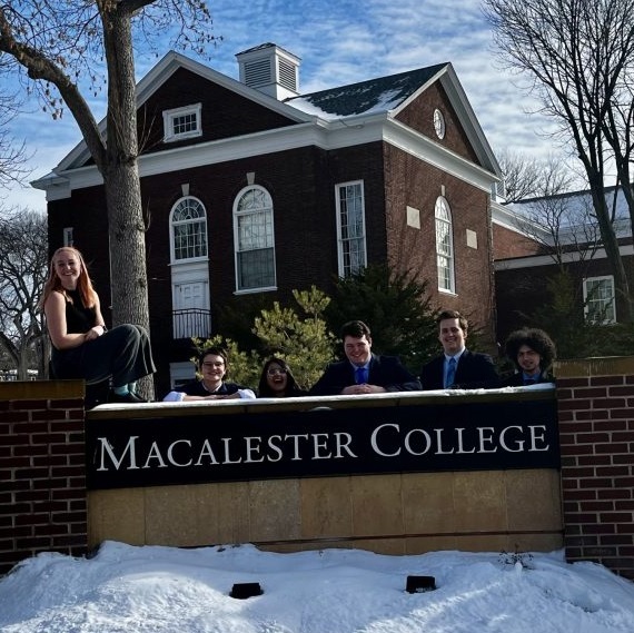 Members of the Ethics/Bioethics Bowl team pose next to a sign that says Macalester College.