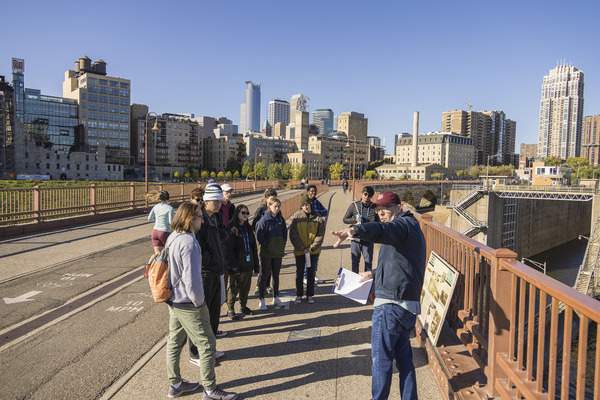 Professor teaches class of students, city skyline visible in the distance