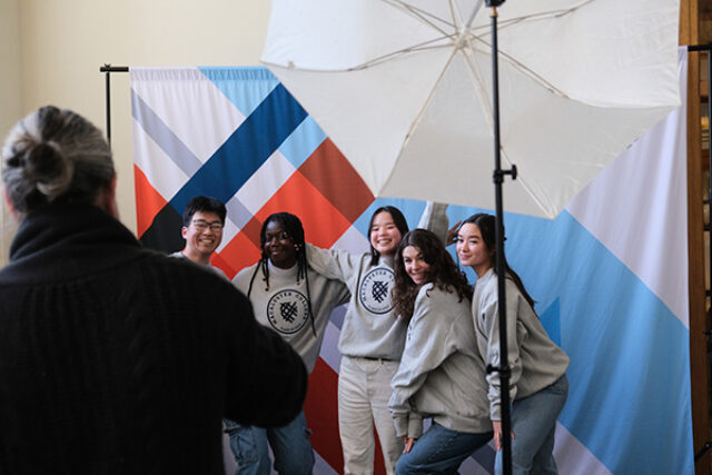 Four students pose for a picture in front of a Macalester backdrop wearing Class of 2023 sweatshirts
