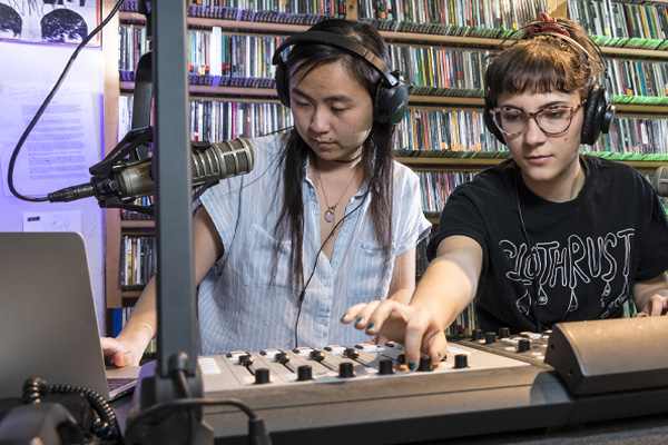 Two students wearing headphones working in a radio station