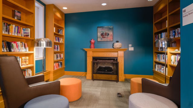 Library reading room fireplace surrounded by cozy chairs and shelves of books.