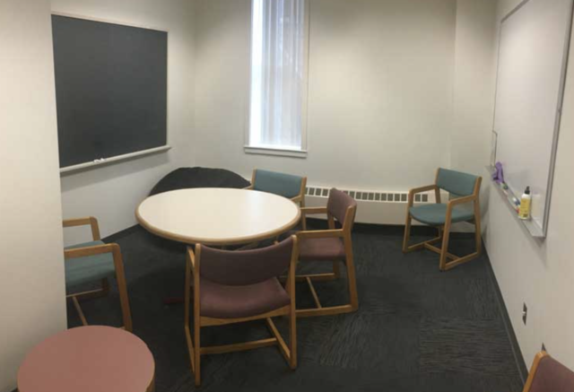 Room with round table, 6 chairs, and a blackboard.