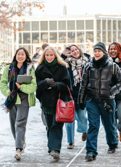Macalester students, all bundled up for winter, walk across campus laughing and talking.