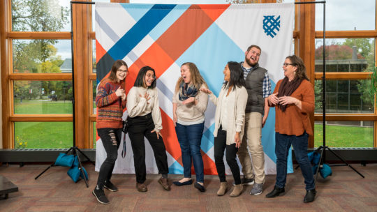Photo of people laughing in front of a Macalester backdrop.