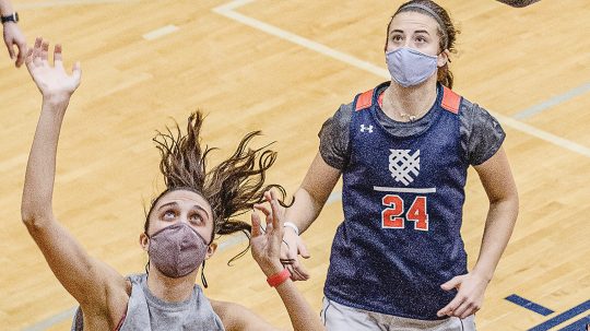 Photo of two students wearing masks and playing basketball