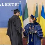 President Suzanne Rivera shakes hands with a graduate as she presents them with their diploma.