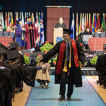 A graduate walks back to their seat with their diploma while high fiving another graduate