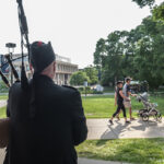 A Macalester piper plays while a couple with a stroller passes by