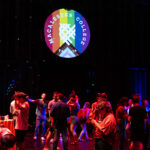 Alumni dance at Scots Pride prom in a dark room with the Scots Pride logo projected on the wall