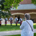 An alum takes a photo on their phone of the Pipe Band playing