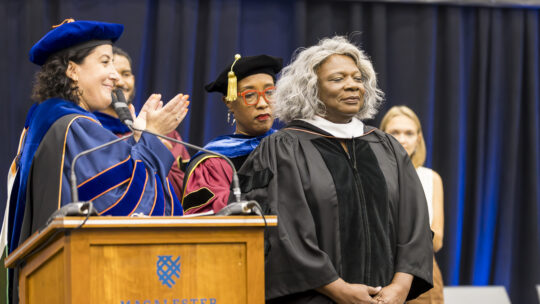 Leona Tate bows her head as she receives her honorary degree. President Rivera, standing to her left, claps.