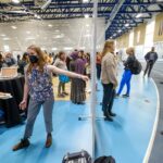 The crowd is visible behind and next to a student presenting a poster at the Summer Research Showcase