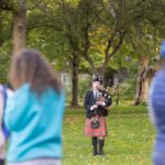 A bagpiper plays while standing on the lawn.