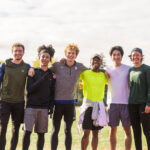Six people smile and pose for a photo outside