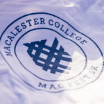 Macalester College shield printed in blue on a white Mac Fest 5K t-shirt