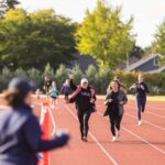 Two people smile and cheer as they run around the outdoor track