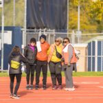 Four people smile and pose for a photo on the outdoor track
