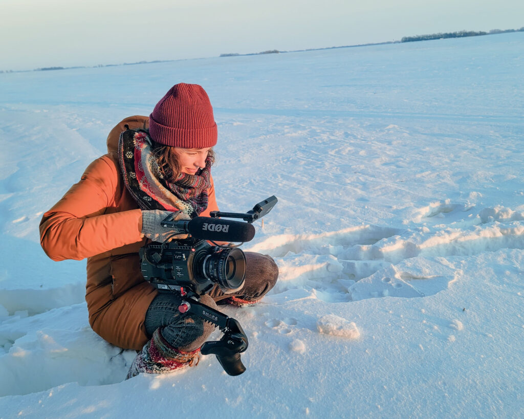 A film maker crouches in the snow with their camera