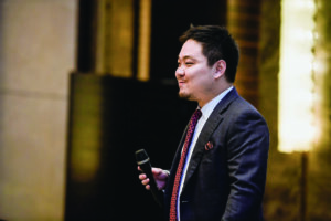Max Wang ’15 speaks at an event, addressing alumni about shared Macalester values and the importance of staying connected.